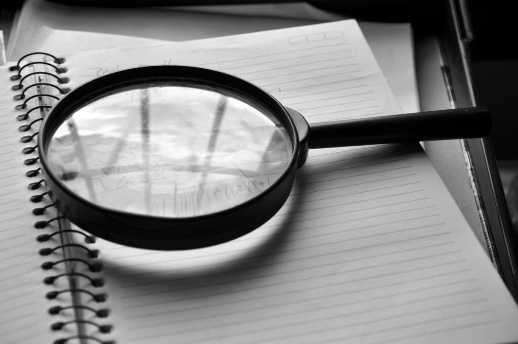 Loupe posée sur un carnet de notes manuscrites, symbole d'analyse et d'observation terrain au cœur de la démarche Lean